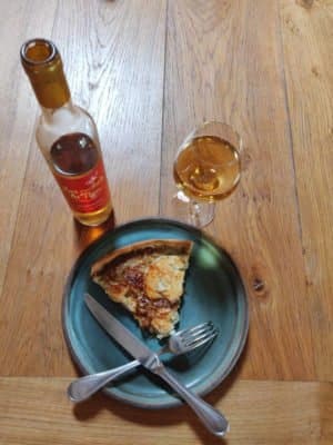 Assiette avec une part de tarte aux oignons, chèvre et miel accompagnée d'un verre d'hydromel.